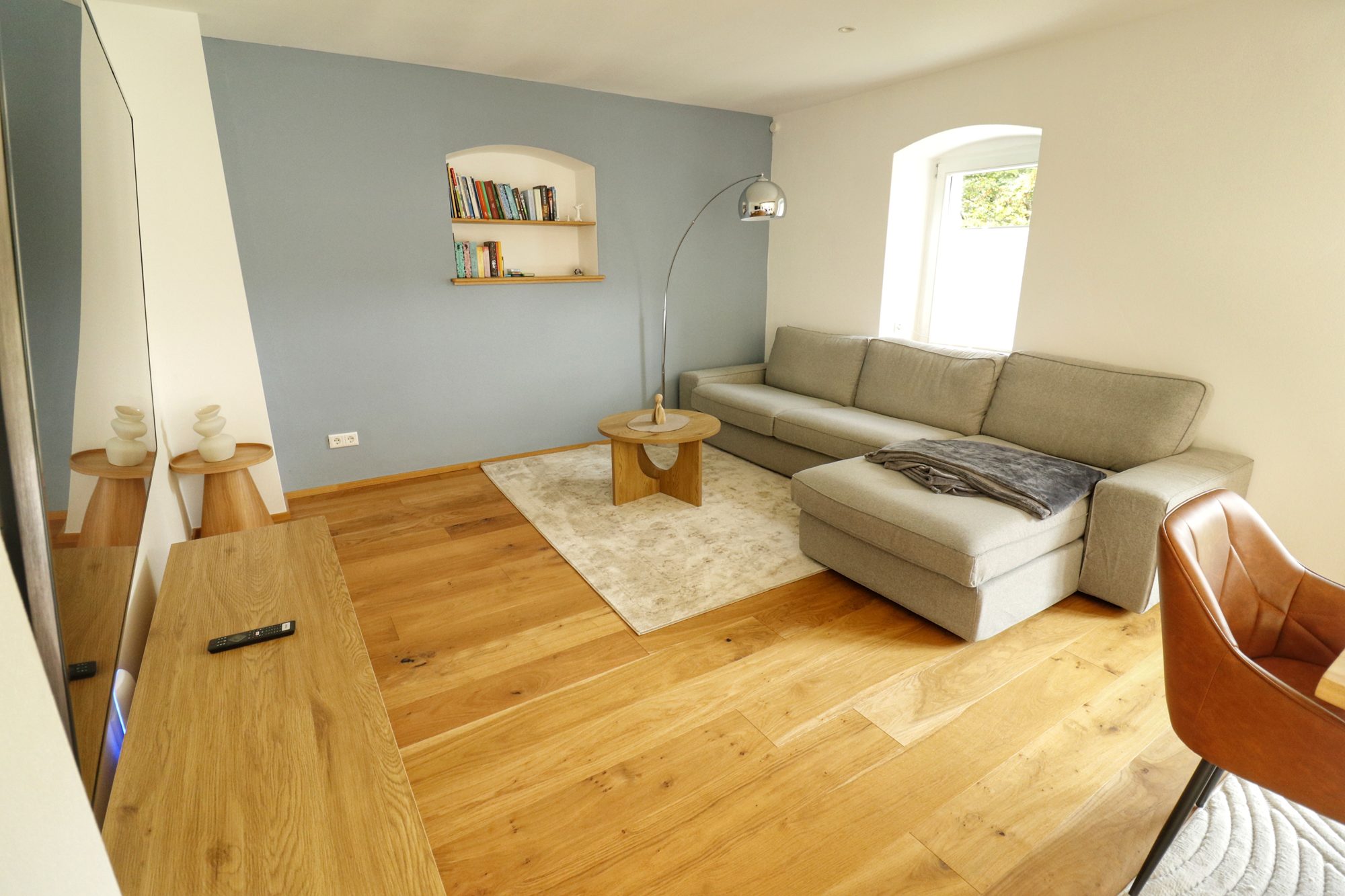 Wohnzimmer der Lodge mit grauem Sofa, Sessel und Blick in den Garten